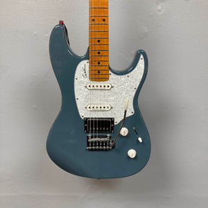 A blue Godin Session T-Pro with Bag electric guitar featuring a white pickguard, H-S-S pickups, whammy bar, and maple neck hangs on a gray wall.