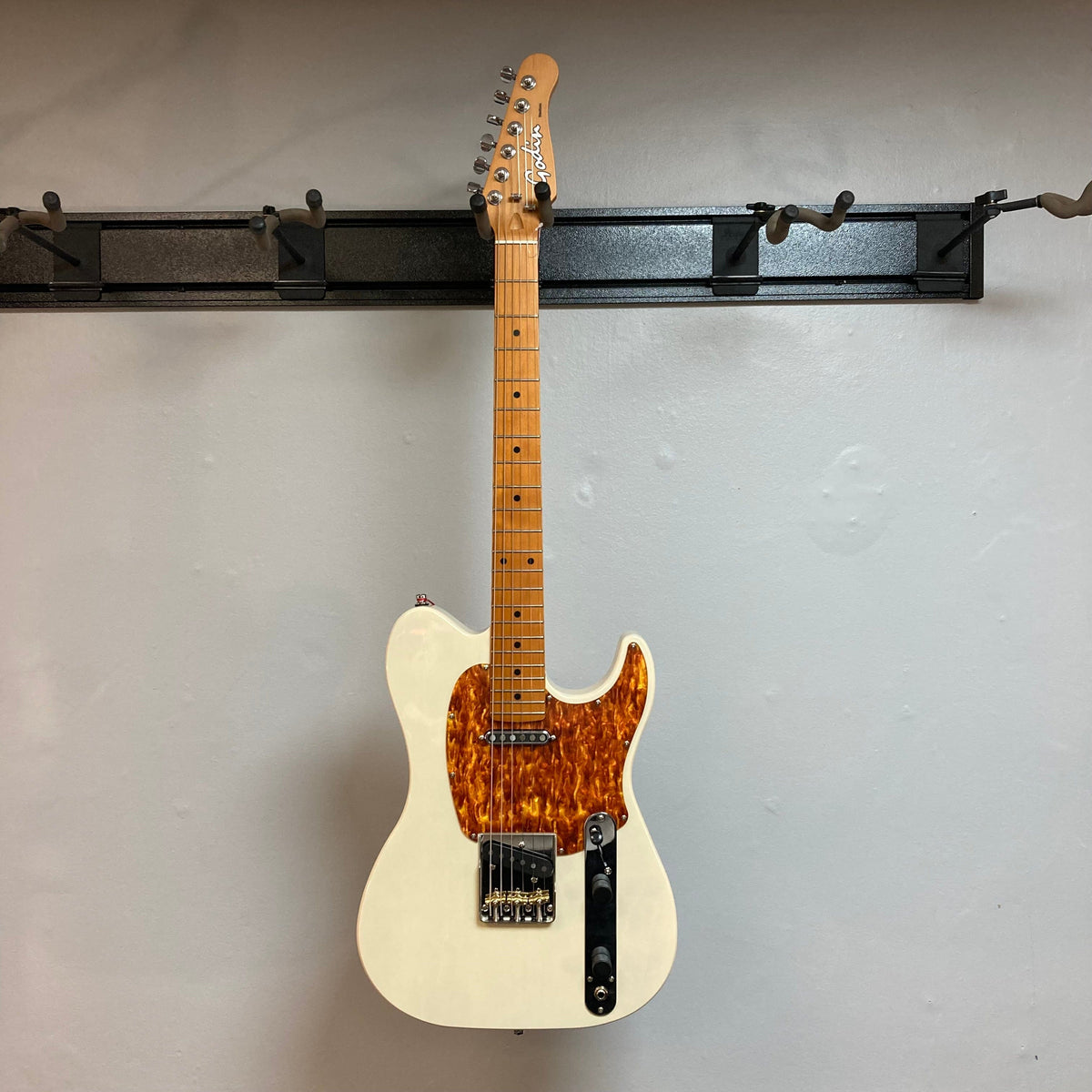 Godin Stadium Pro Ozark Cream MN Electric Guitar displayed on a wall, featuring a high-gloss finish and exceptional pickups for versatile musical styles.