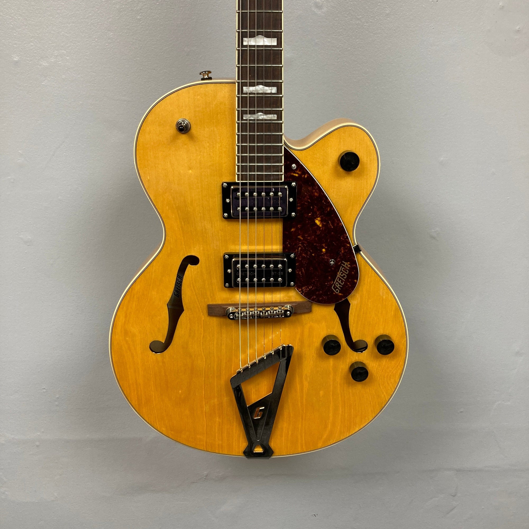 Gretsch G2420 Streamliner Village Amber guitar displayed on wall, highlighting its strings and body design. Ideal for enthusiasts seeking quality sound and craftsmanship.