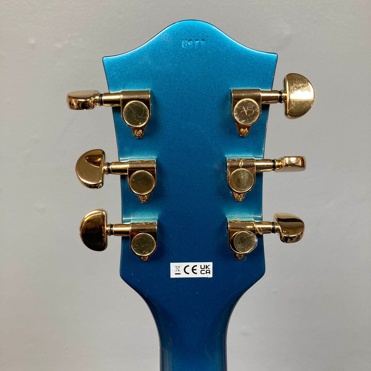 Back of a Riviera Blue Gretsch G2655TG Streamliner Refurb semi-hollow electric guitar headstock featuring six gold tuning pegs and a white sticker with certification symbols.
