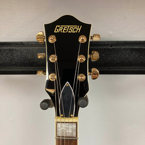 Close-up of a Gretsch G2655TG Streamliner Riviera Blue Refurb guitar headstock with gold tuning pegs and the Gretsch logo, set against a plain wall background.