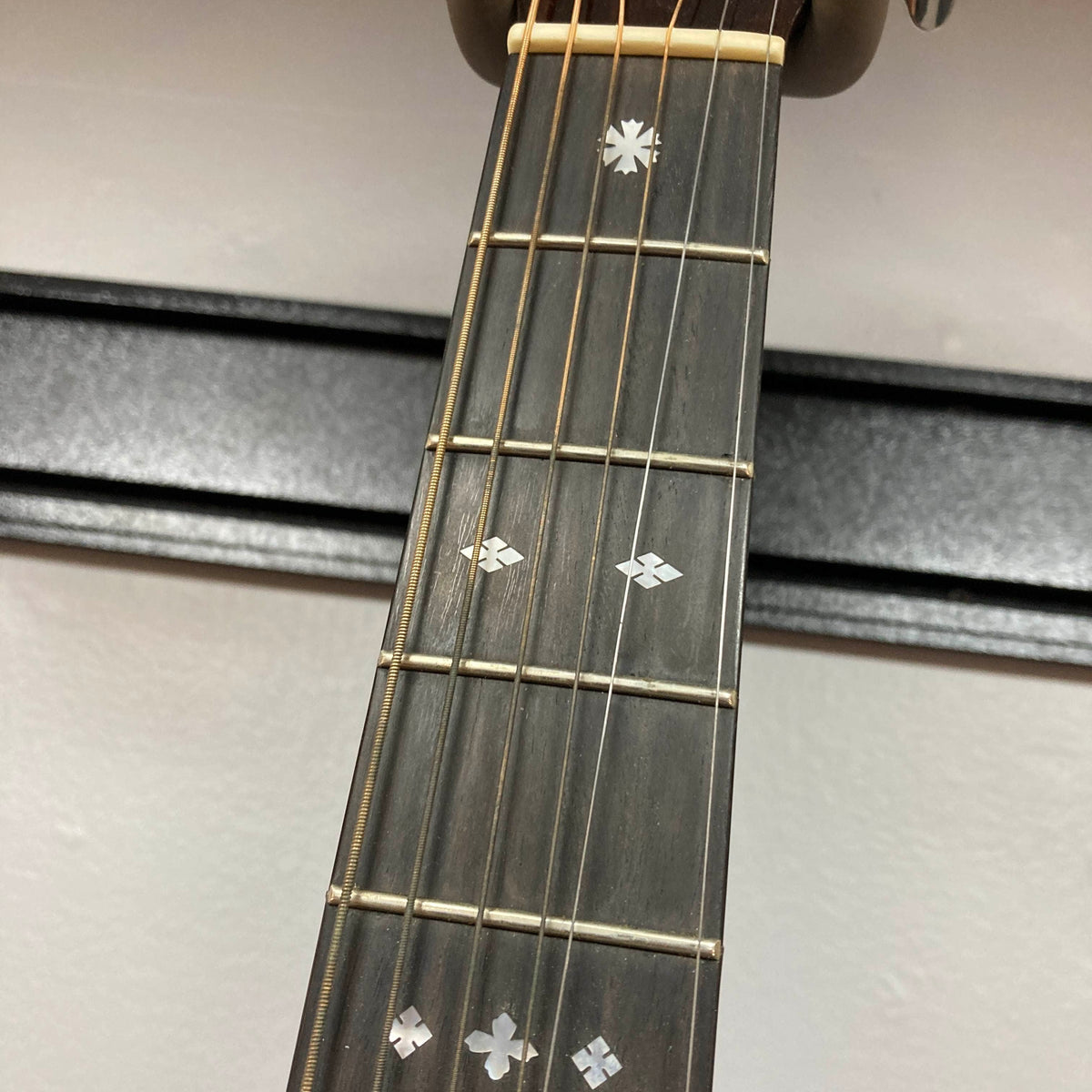 Close-up of the Guild Gad-30reasb w/Case guitar neck, featuring strings, frets, and decorative inlays on a solid Indian rosewood fingerboard, set against a white wall background.