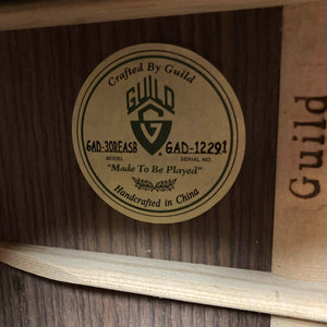 A close-up of a Guild Gad-30REASB w/Case guitar label inside the body displays the model GAD-30REASB, serial number GAD-12291, and the phrase "Made To Be Played," indicating this orchestra-sized acoustic-electric guitar by Guild was handcrafted in China with solid Indian rosewood back and sides, and is equipped with a premium Fishman Matrix pickup.