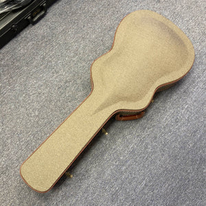 A Guild Gad-30reasb acoustic-electric guitar crafted from solid Indian rosewood rests inside its closed, tan-colored Guild case with brown trim on a gray carpeted floor.