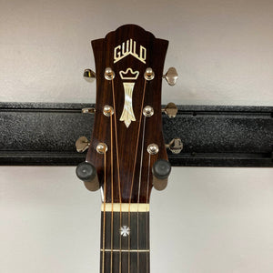 Headstock of a Guild Gad-30reasb acoustic-electric guitar, crafted from solid Indian rosewood, featuring tuning pegs and a decorative inlay, mounted on a wall hanger.