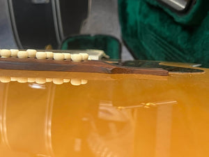 Close-up side view of a Guild USA F-512 w/OHSC 2005 Circa 12-string guitar, showing the bridge slightly lifting from the body with its reflection visible on the surface.