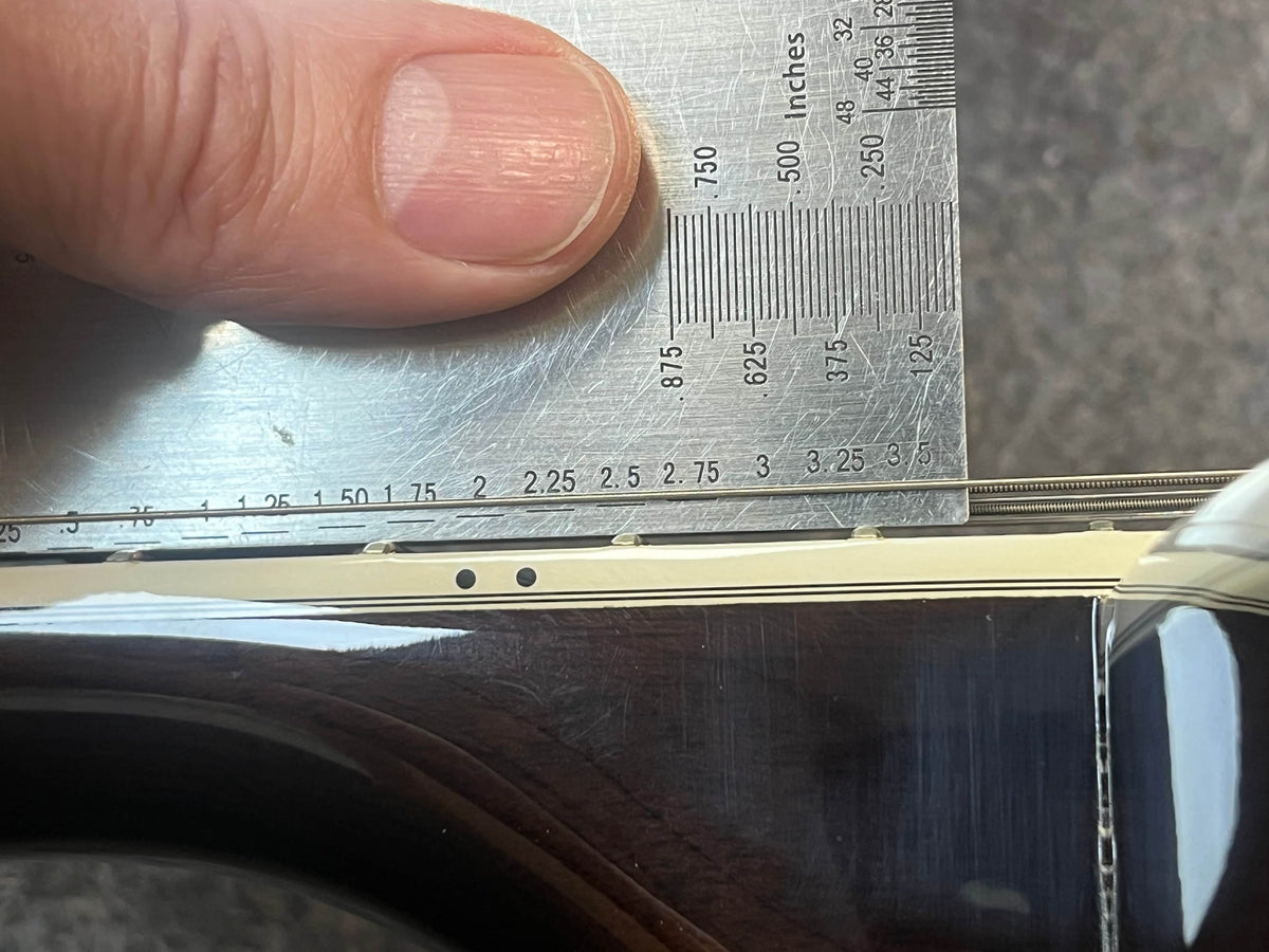 A ruler is held vertically against the strings and fretboard edge of a Guild USA F-512 w/OHSC 2005 Circa guitar, measuring the string height above the fretboard.
