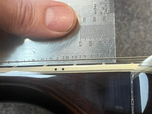 A ruler is held vertically against the strings and fretboard edge of a Guild USA F-512 w/OHSC 2005 Circa guitar, measuring the string height above the fretboard.