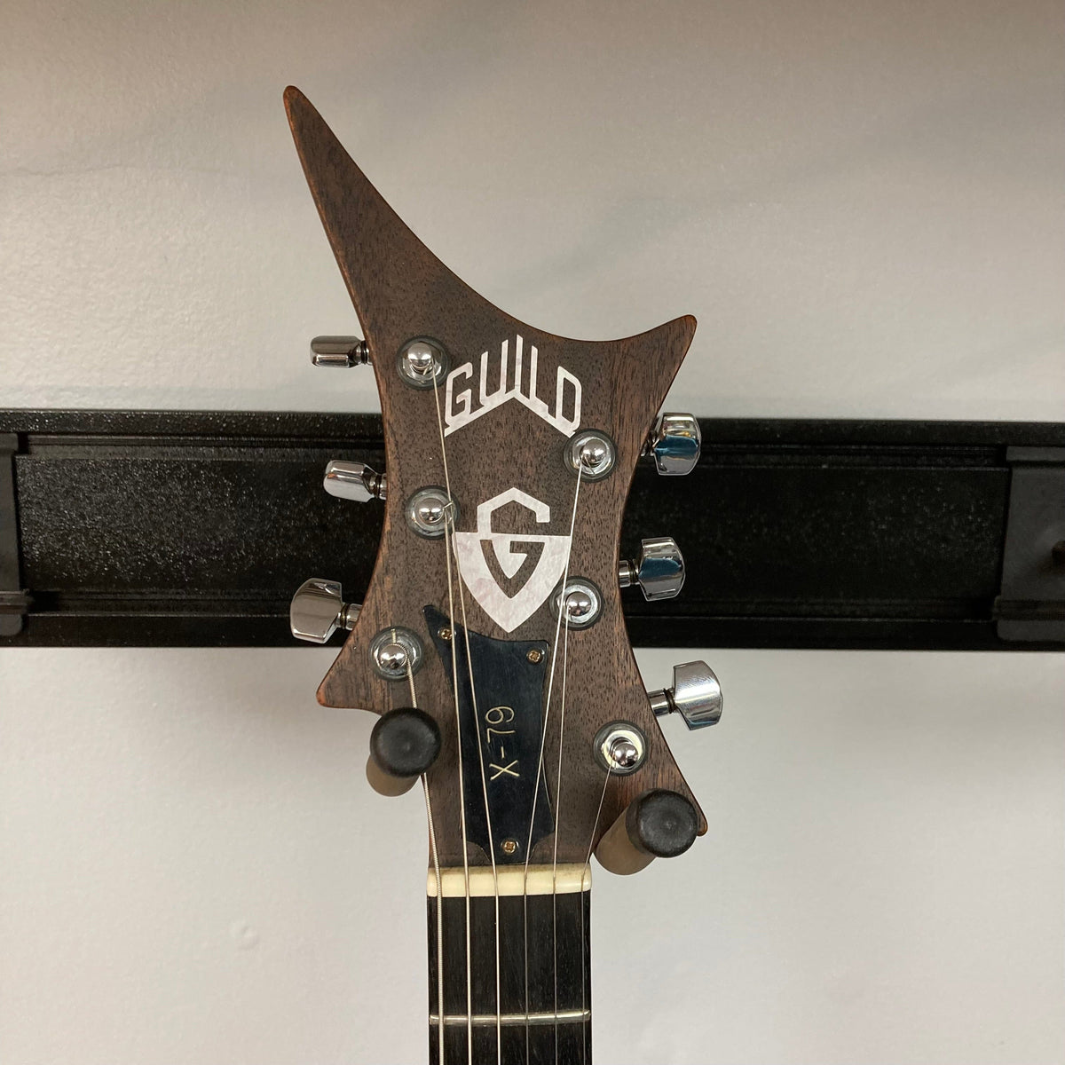 Guild USA X-79 Candy Apple Red guitar, 24-fret fingerboard, avant-garde body, professionally refinished, mounted on a wall with visible neck and logo.