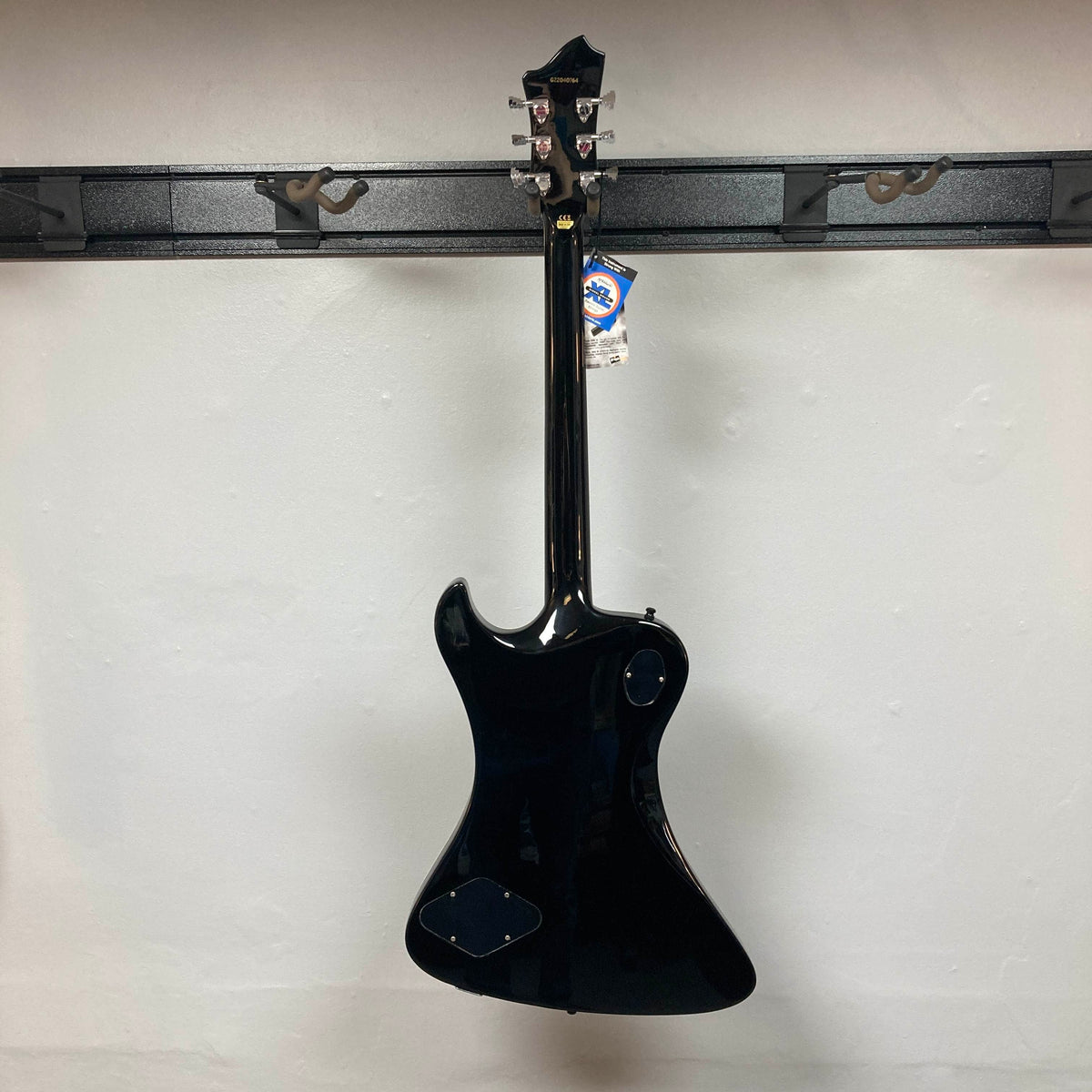 A Hagstrom Fantomen Custom Black w/case electric guitar by Hagstrom hangs on a wall rack, displayed from the back with a tag attached to the headstock.