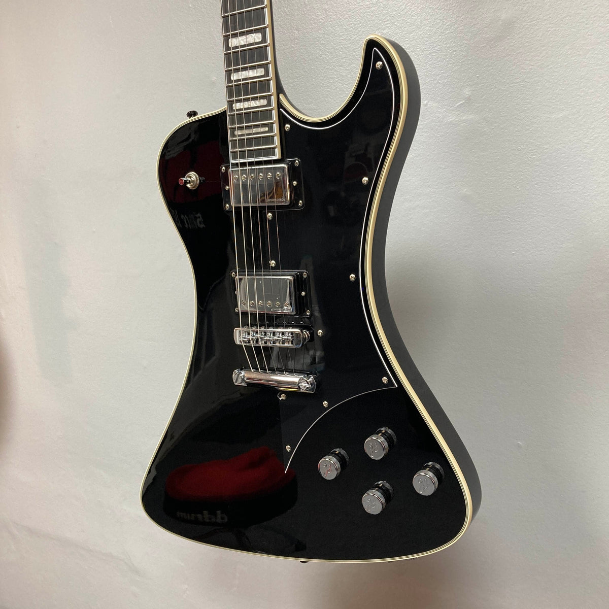 The Hagstrom Fantomen Custom Black w/case electric guitar by Hagstrom features a glossy black finish, cream binding, chrome hardware, a pair of Lundgren Design humbuckers, four control knobs, and a three-way pickup selector switch. It is displayed hanging against a white wall.