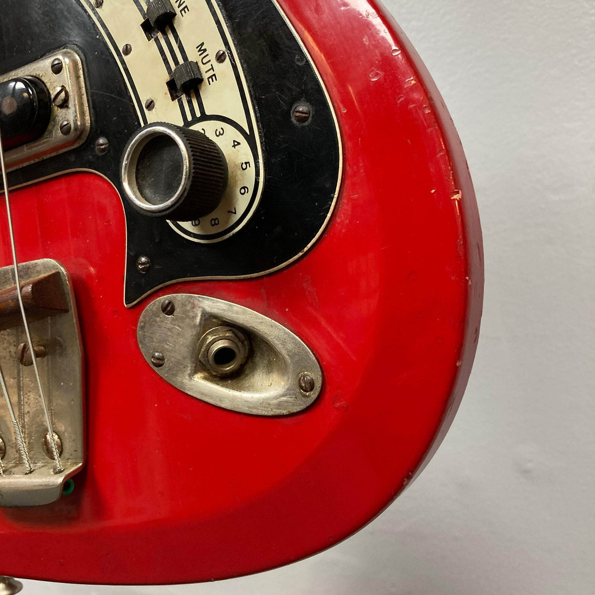 Hagstrom HII-B Mid-1960s Red Medium-Scale Bass, close-up of control plate, showing volume knob, mute slider, output jack, tailpiece, and strings.