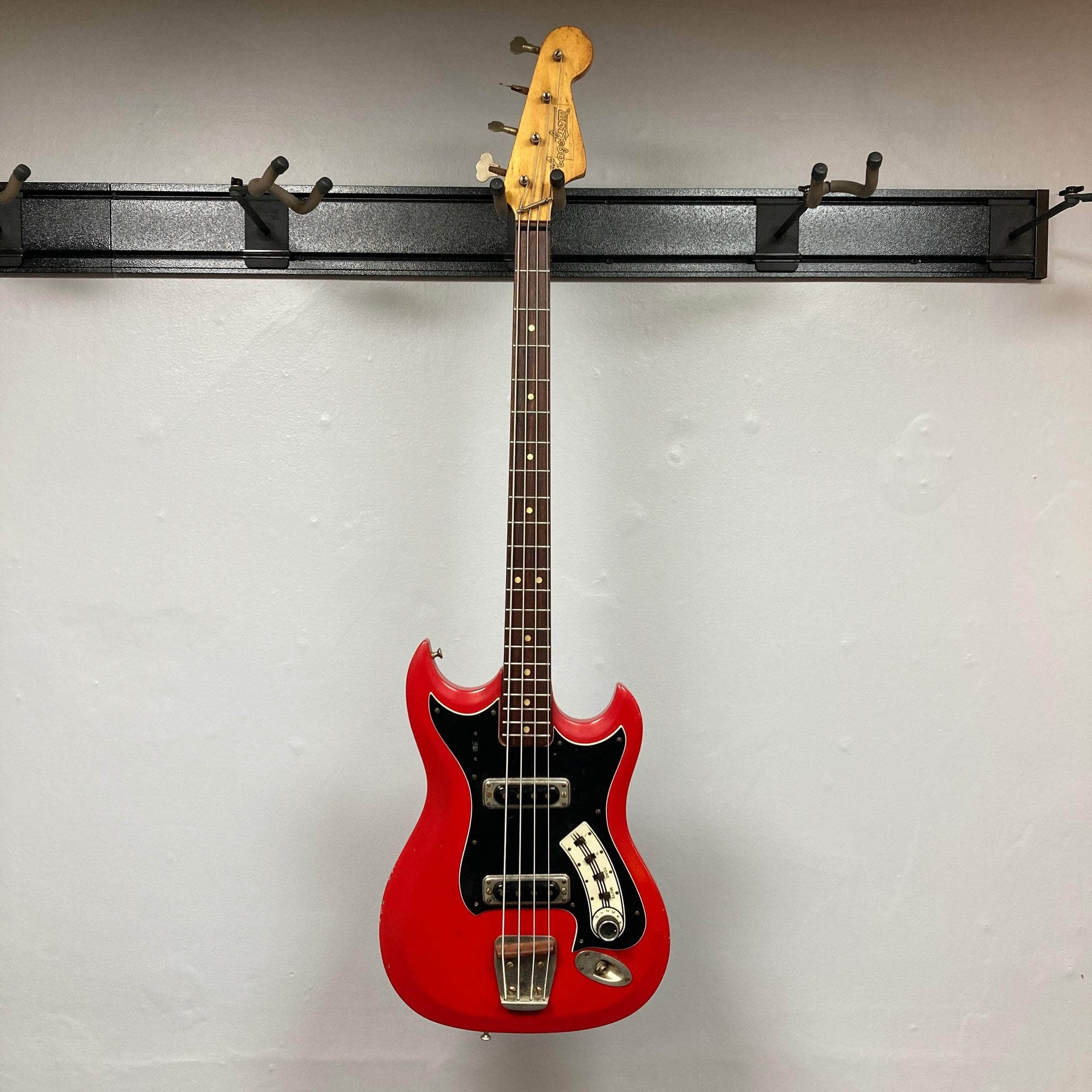 Hagstrom HII-B Mid-1960s Red Medium-Scale Bass, features dual pickups, distinctive design, vintage character, hanging against a light-gray wall.
