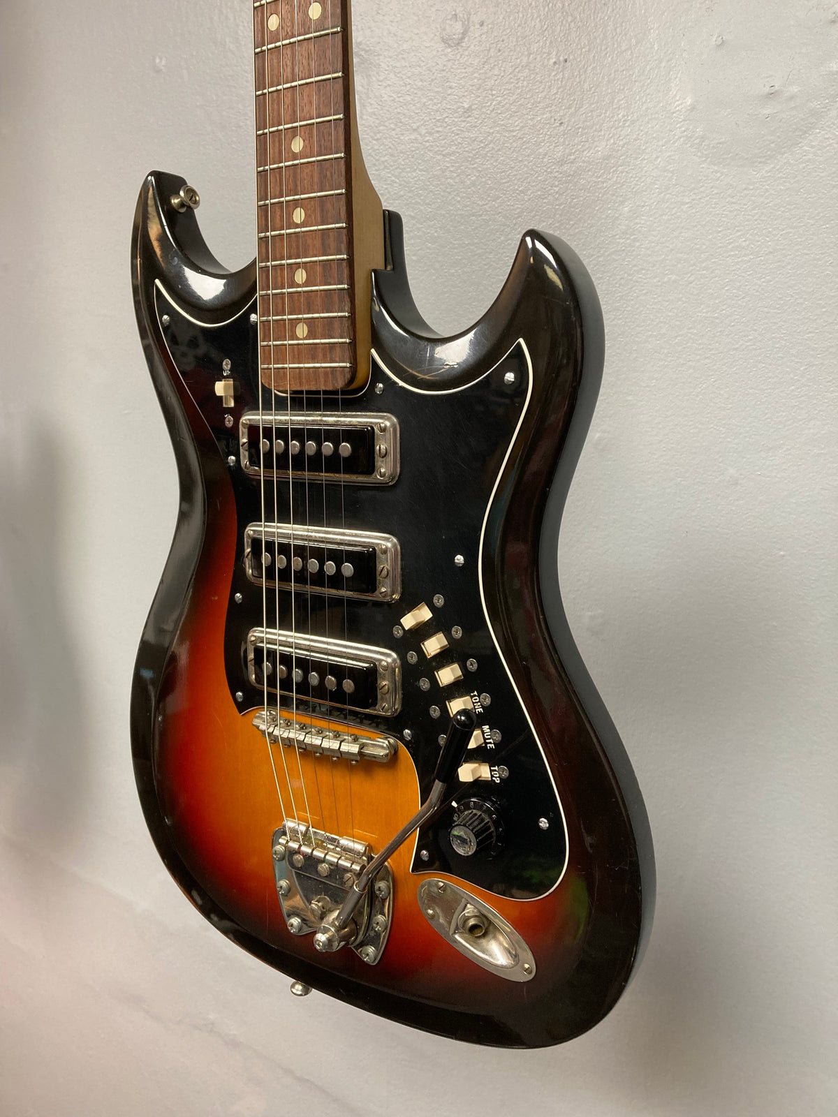 Hagstrom III 1960s Sunburst electric guitar with original case, displayed on a wall, showcasing close-up details of strings and body.