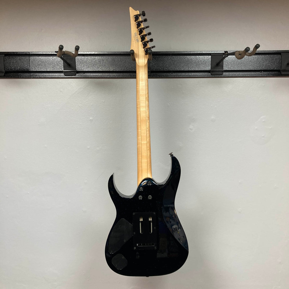 A Cosmic Blue Ibanez Prestige RG1570 electric guitar by Ibanez, shown hanging on a wall mount from the back, displays its tuning pegs, electronics cavity cover, and signature Wizard Prestige neck. Includes case.