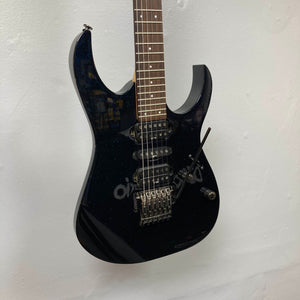 An Ibanez Prestige RG1570 electric guitar in Cosmic Blue with a case, featuring a double-cutaway body, three pickups, and a Wizard Prestige neck, hangs on a white wall.