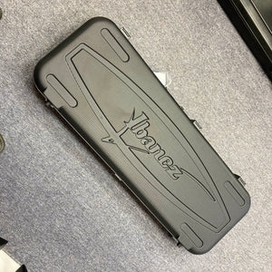 An Ibanez Prestige RG1570 Cosmic Blue guitar with a black hard case featuring the Ibanez logo, ideal for this Japanese-made model, is shown resting on a gray carpeted floor.