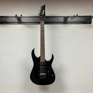 An Ibanez Prestige RG1570 Cosmic Blue electric guitar with case sits on a wall-mounted rack against a plain white wall, highlighting its vivid blue finish and signature Wizard Prestige neck.