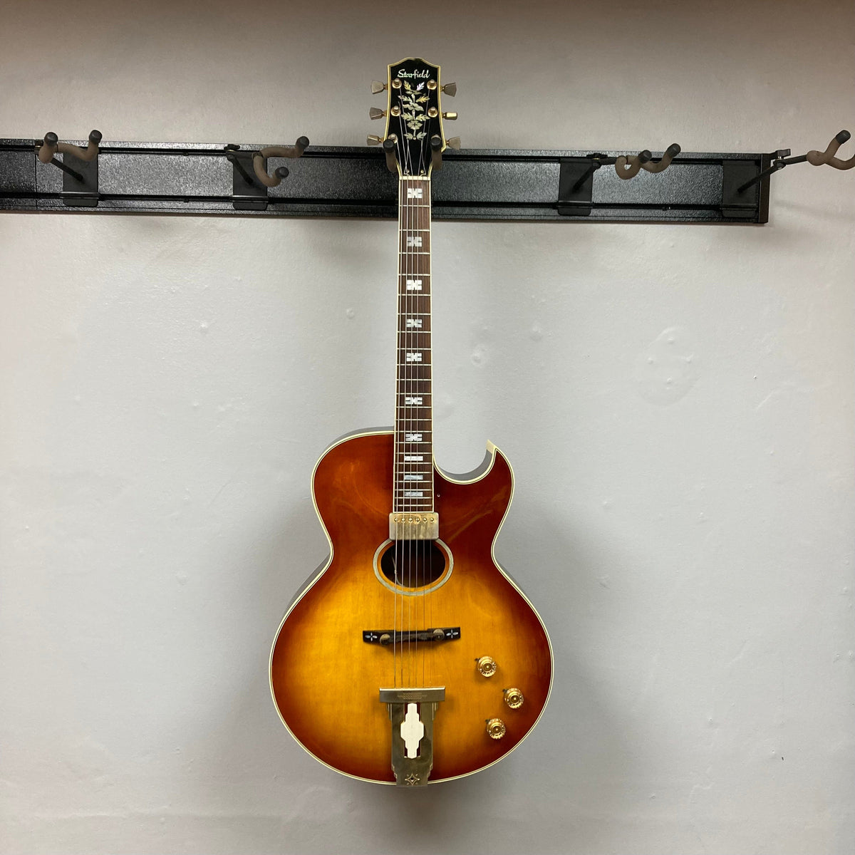 Ibanez Starfield hollow body guitar with case, featuring a classic design, humbucker neck pickup, and vintage headstock, displayed on a wall.