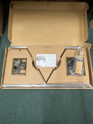 Opened cardboard box containing disassembled parts of an Atlas Sound SB36W Professional Studio Boom Microphone Stand, some wrapped in plastic and bubble wrap, placed on a green carpet.
