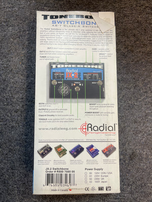 Back of a preowned Radial Engineering Tonebone Switchbone JX-2 AB-Y Class-A Switcher, showing product details, specs, and diagrams for its AB-Y amp switching and transformer-isolated output on a gray surface.
