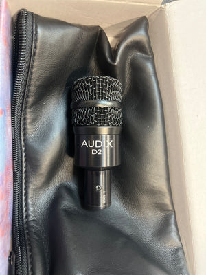 A preowned Audix D2 Hypercardioid Dynamic Instrument Microphone in black rests on a black zippered pouch inside its cardboard box.