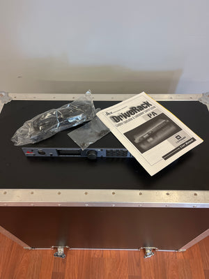 Dbx DriveRack PA Complete Loudspeaker Management System by dbx, with power cable, mounting brackets, and user manual, displayed on a black case with metal edges on a wooden floor.