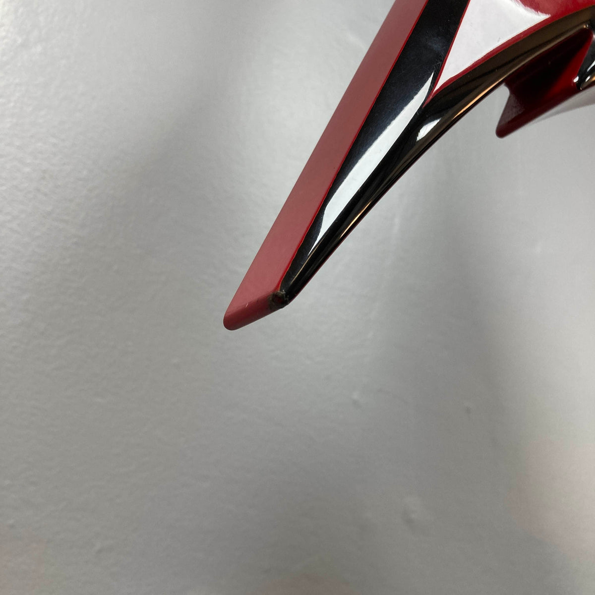 Close-up of a shiny red and black Jackson Phil Demmel Demmelition King V electric guitar with a pointed edge, set against a plain light gray background, showcasing its iconic Floyd Rose tremolo system.