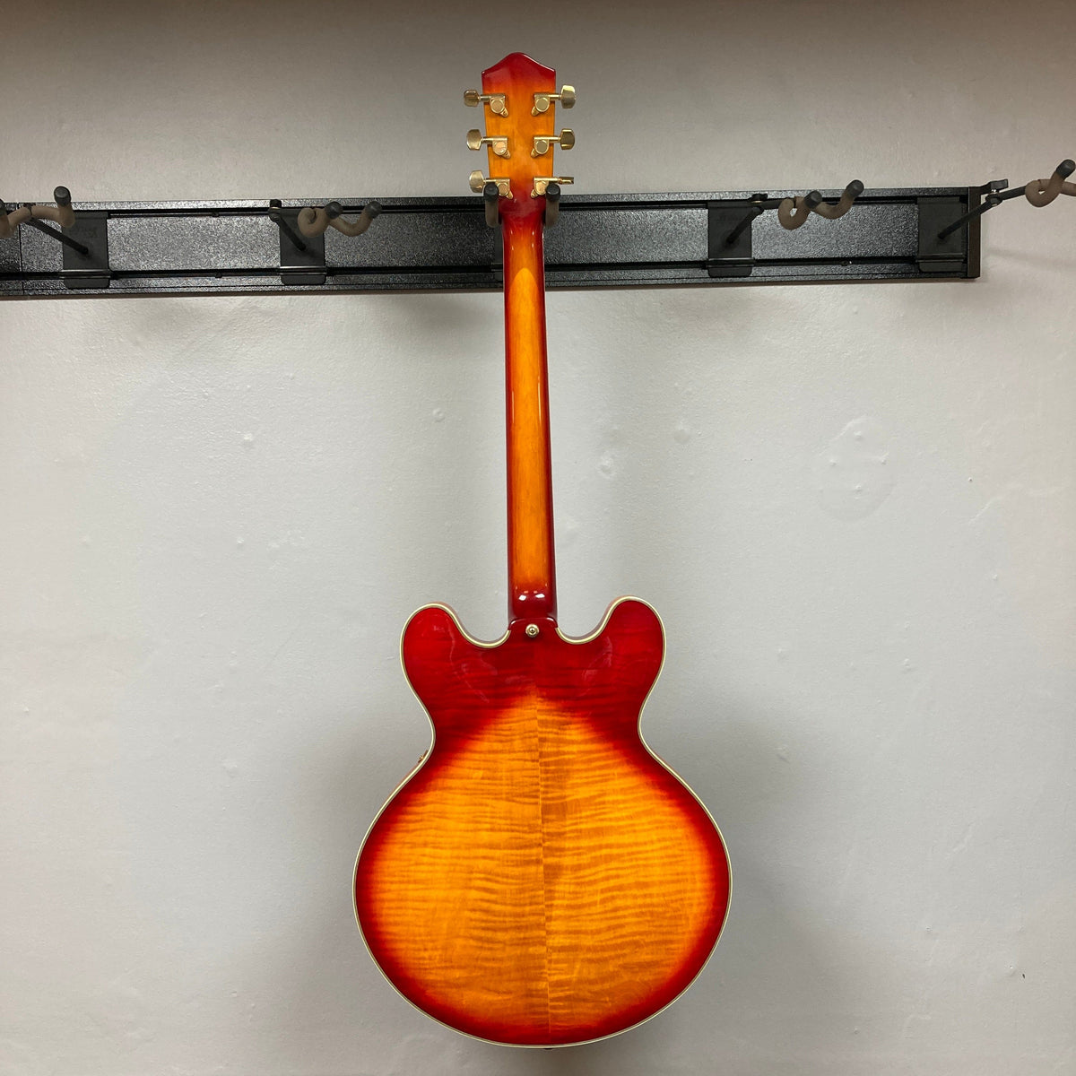 Johnson JH-250-C Semi Hollow Cherry Burst guitar hanging on a wall, showcasing its elegant design and craftsmanship, ideal for music enthusiasts.