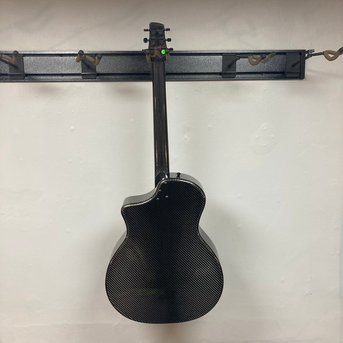 KLOS Grand Cutaway Acoustic Guitar w/Fishman Sonitone Piezo, carbon fiber body, hanging on a wall, showcasing its sleek design and advanced features.