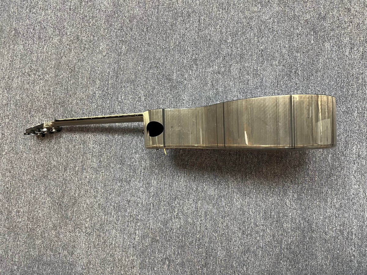 A side view of the Klos Grand Cutaway AE w/Fishman acoustic ukulele rests on a gray carpet, showcasing the body and neck of this premium Klos instrument.