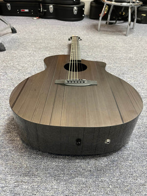The Klos Grand Cutaway AE w/Fishman, a black acoustic guitar by Klos, rests on a gray carpeted floor with instrument cases and a stool in the background.