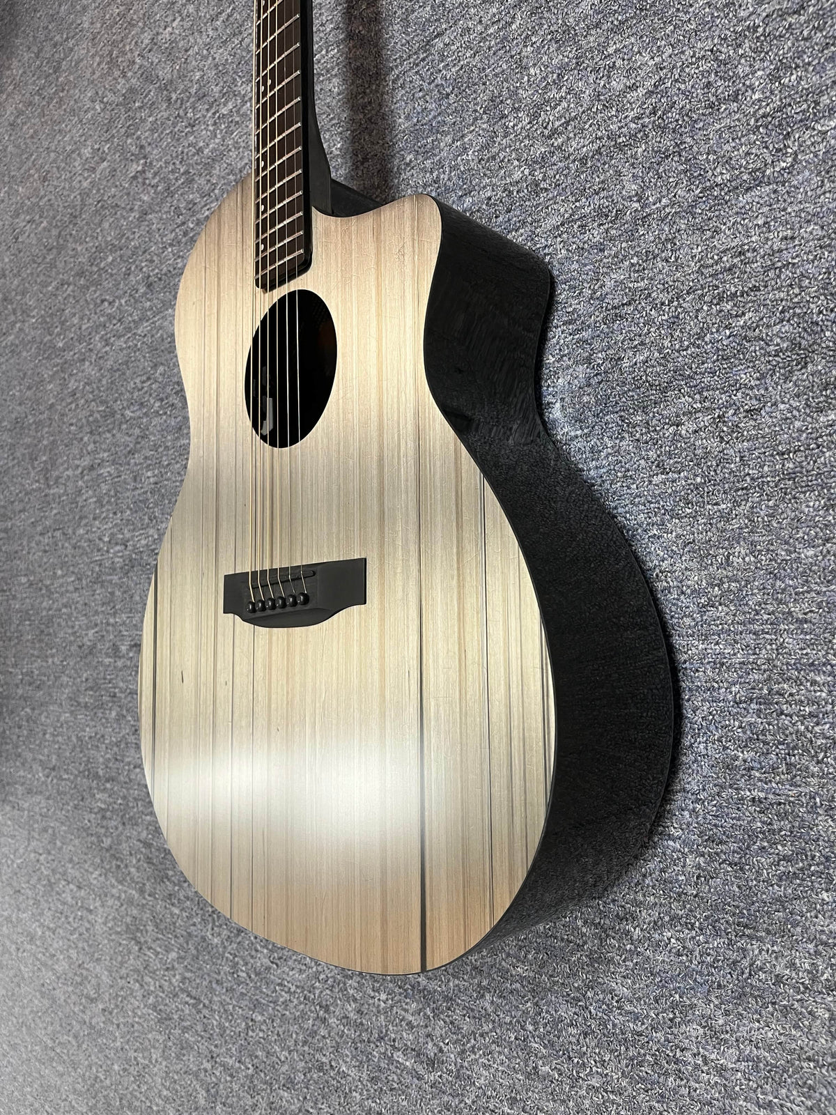 The Klos KLOS Grand Cutaway AE w/Fishman acoustic guitar, with a light wood top and black sides, stands upright on a gray textured surface.