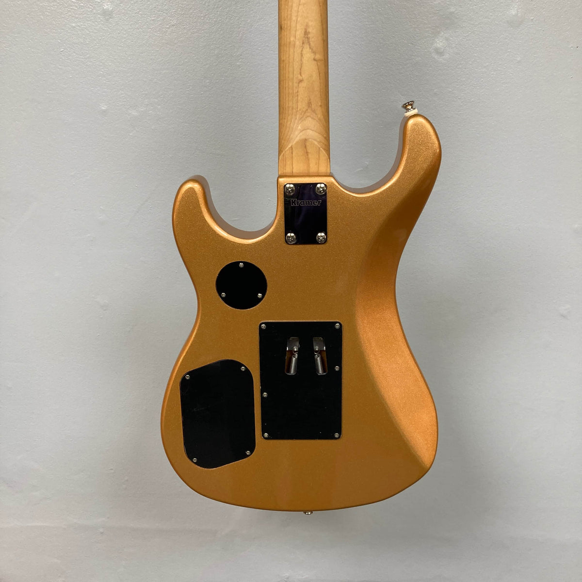 The image shows the back of a Kramer 84 HH Killswitch electric guitar in Smoked Almond Metallic with a natural wood neck, black cover plates, and round and rectangular panels, set against a plain light gray wall.