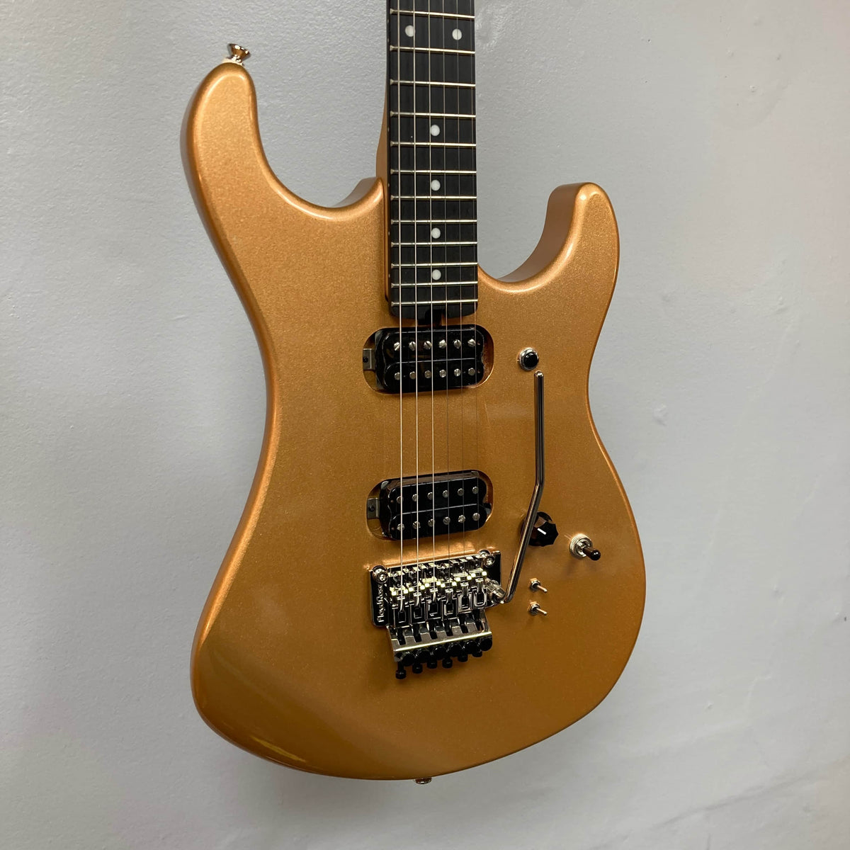 A Kramer 84 HH Killswitch electric guitar in Smoked Almond Metallic with dual humbuckers, Floyd Rose tremolo, and black knobs hangs against a plain light wall. Includes gigbag.