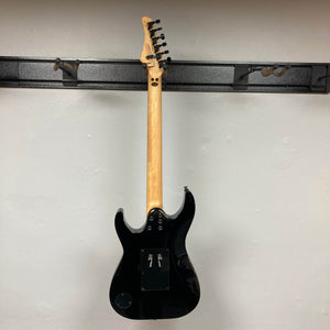 A Kramer Volante Quilt HSFR electric guitar in Aqua Burst, shown from the back, hangs on a wall rack. Its wooden neck, tuning pegs, and back panel covers are visible against a plain light wall. No strings or strap attached. Includes gigbag.