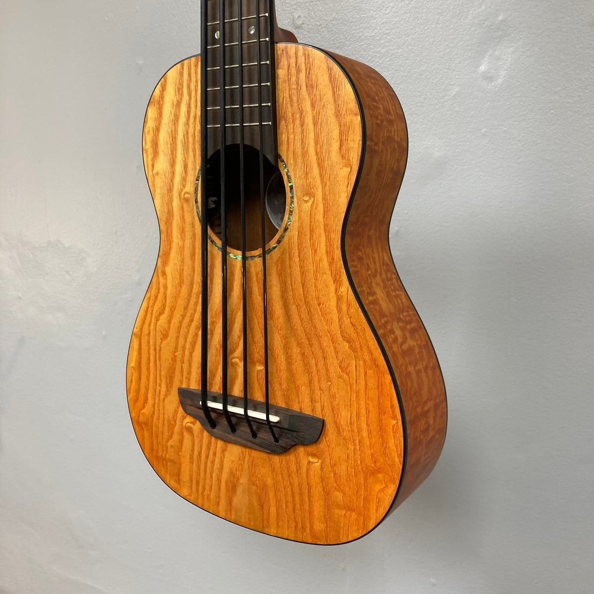 Close-up of Luna Bari-Bass Quilt Ash Top Bass Ukulele with Preamp, showcasing detailed craftsmanship and strings. Includes branded gigbag.