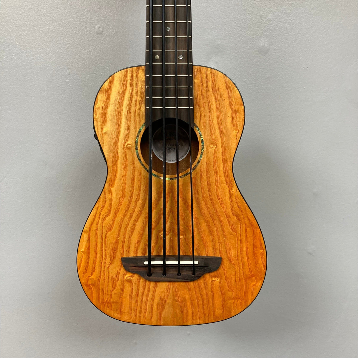 Close-up of Luna Bari-Bass Quilt Ash Top Bass Ukulele with Preamp, showcasing its detailed craftsmanship and strings, accompanied by a branded gigbag.