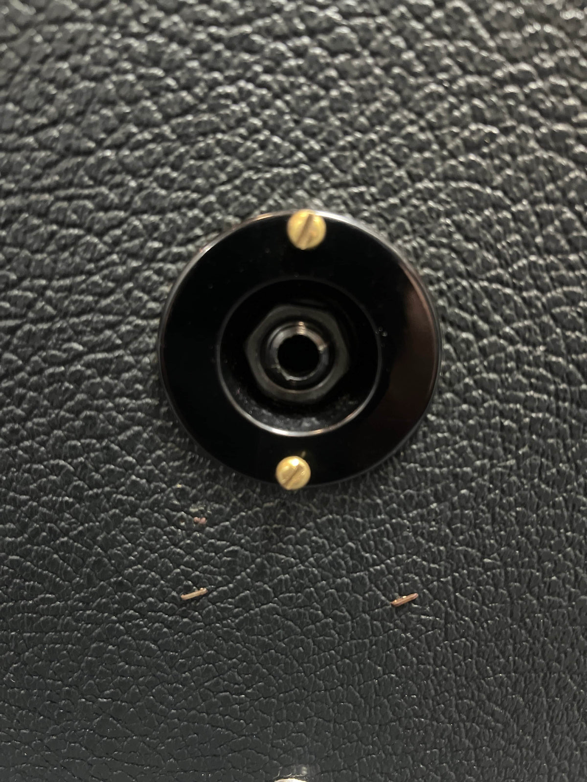 Close-up of a black audio jack socket with gold screws on a textured surface, as found on a 1969 Marshall 4x12 Cabinet with Matching Celestion T1281 Greenbacks.