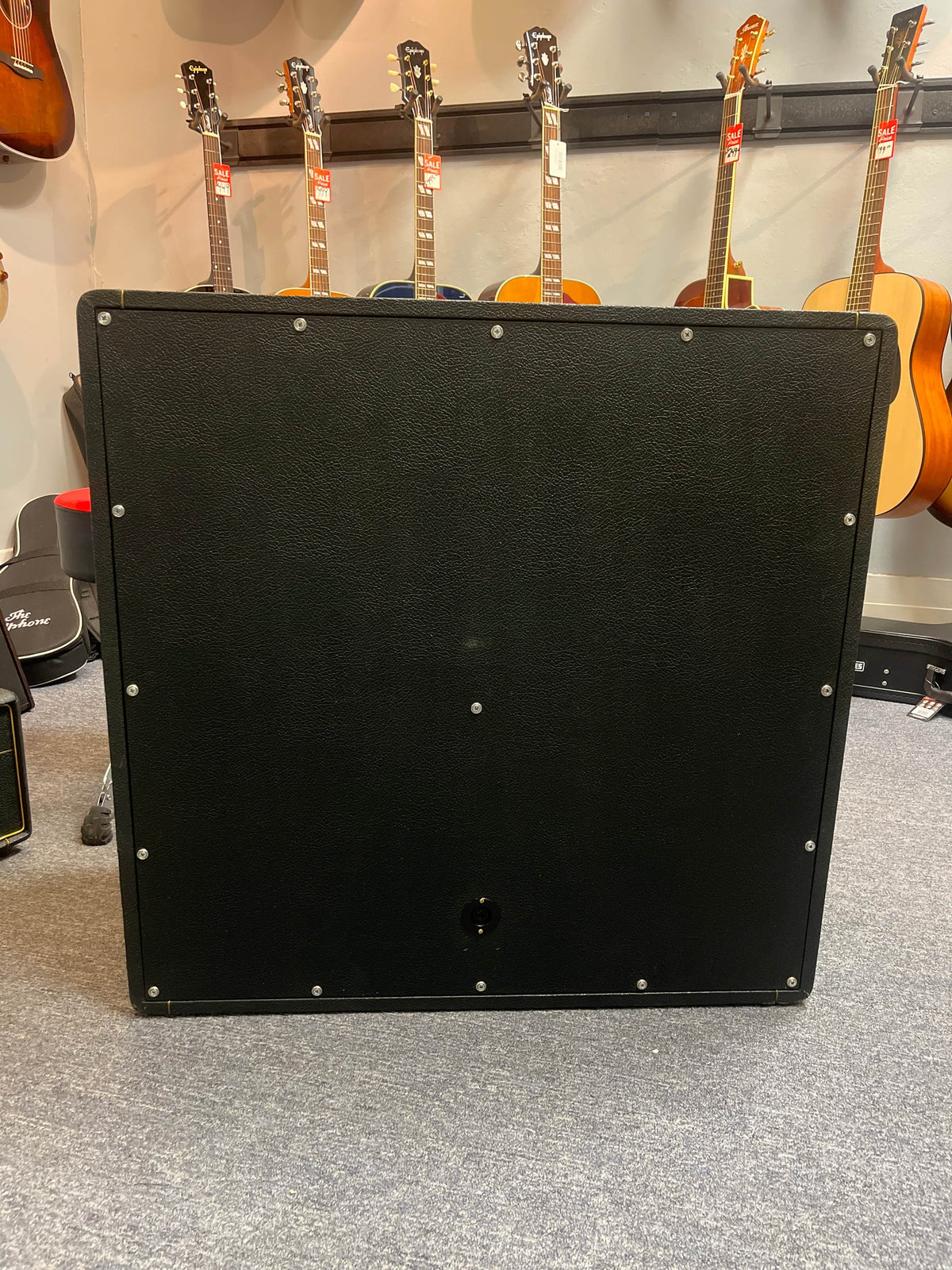 A 1969 Marshall 4x12 Cabinet with Matching Celestion T1281 Greenbacks sits in front of several acoustic guitars on display in a music store.