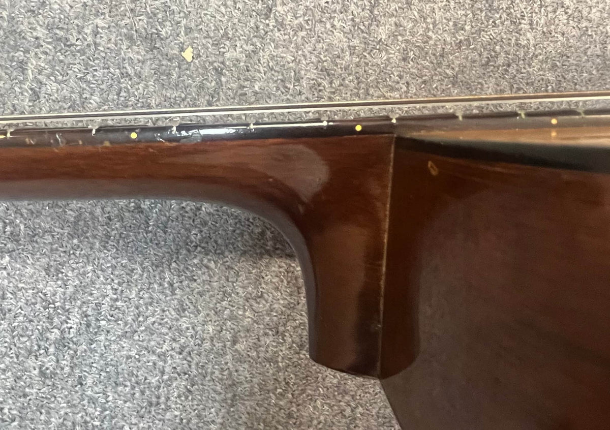 Close-up of the neck joint on a Martin 00-18G Classical Guitar (c. 1961–1962) by Martin, showing some wood wear; the nylon string guitar rests on a gray carpet.