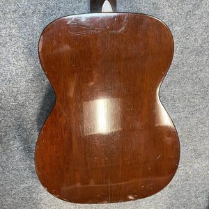 Back of a Martin 00-18G Classical Guitar (c. 1961–1962) with glossy wood finish, showing visible scratches and scuffs, set on a gray textured surface.