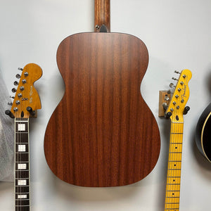Back view of a Martin 00X1AE Acoustic-Electric Guitar mounted on a wall between two electric guitar headstocks.