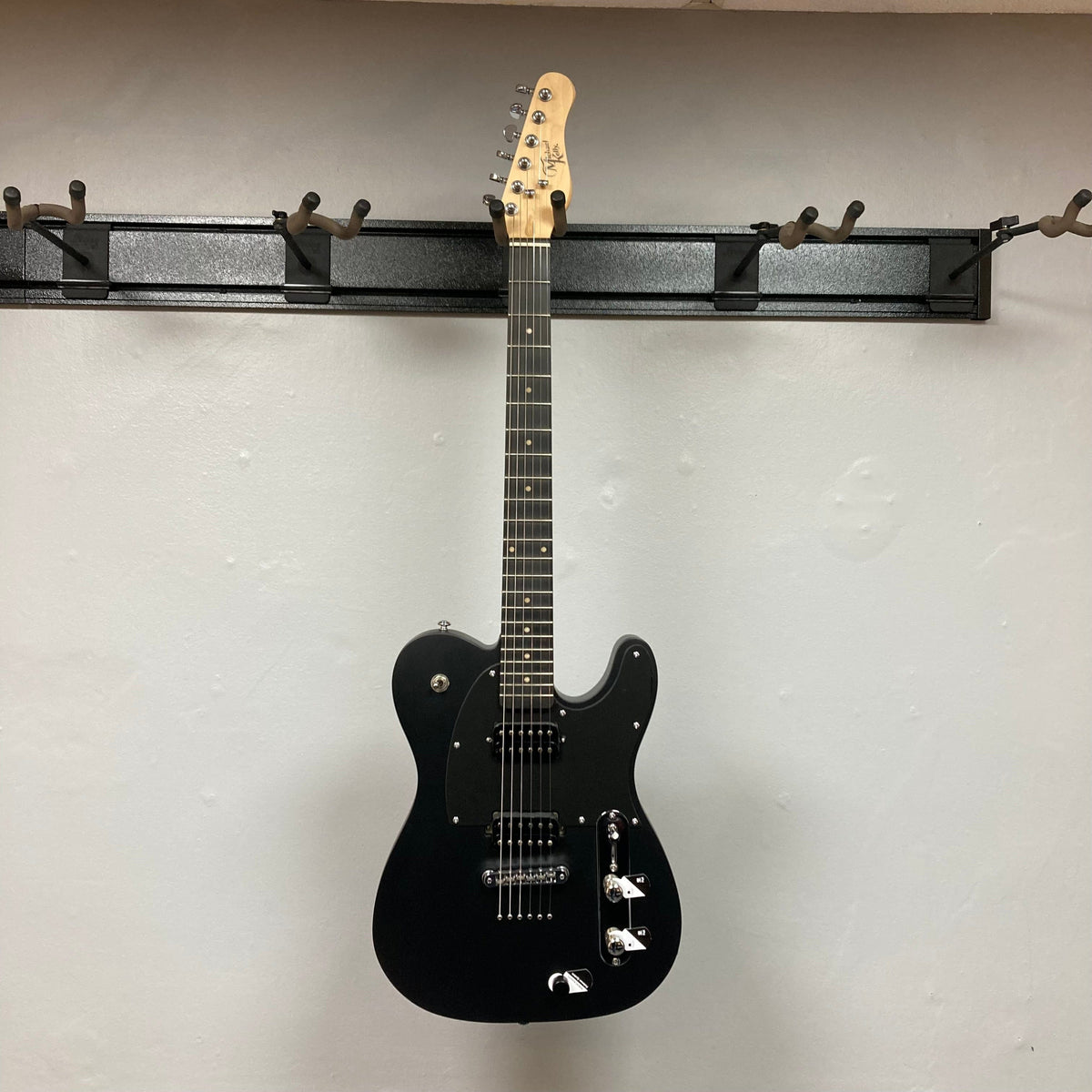 Michael Kelly Hybrid 55T Black Satin Blem electric guitar with dual humbucker pickups and Fishman Powerbridge, displayed on a wall.