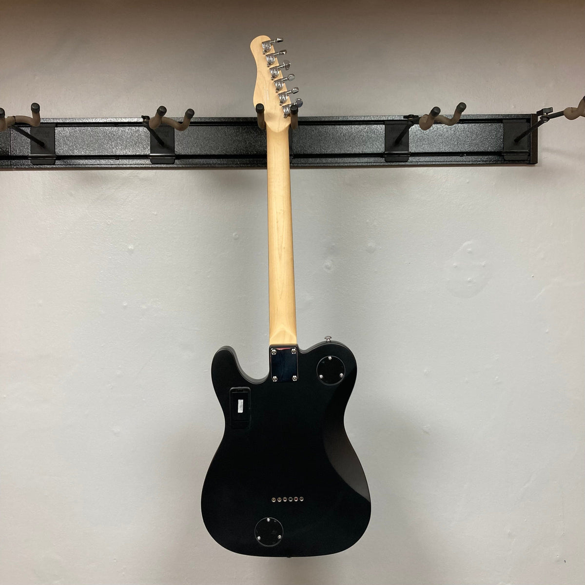 Michael Kelly Hybrid 55T Black Satin Blem, a versatile electric guitar with humbucker pickups and acoustic tones, displayed on a wall hook.