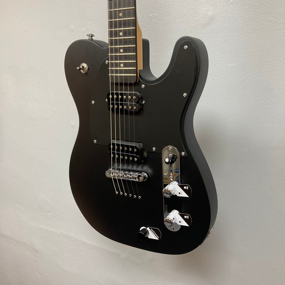 Michael Kelly Hybrid 55T Black Satin Blem electric guitar with silver hardware, displayed against a white wall.