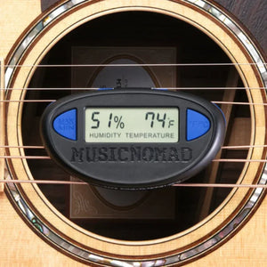 The Music Nomad The Humitar ONE – Acoustic Guitar Humidifier & Hygrometer displays 51% humidity and 74°F inside an acoustic guitar's soundhole, with the "Music Nomad" brand clearly visible on the device front.