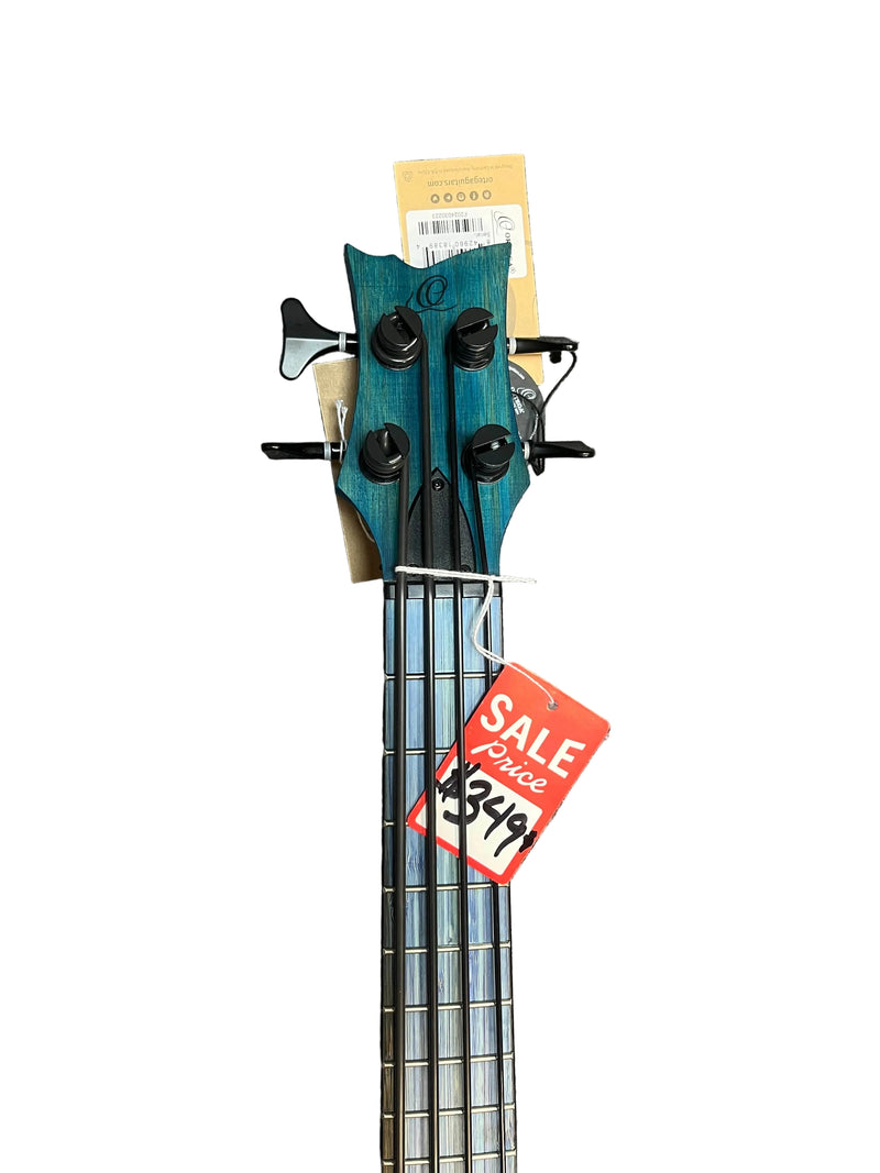 An Ortega RUSWB-UB Uke Bass Stonewashed with a vintage finish and f-hole design rests on a gray carpet; this Ortega instrument features a red sale tag on its headstock.