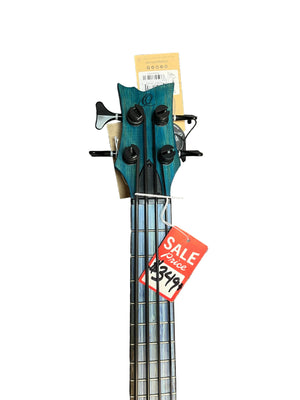 The Ortega RUSWB-UB Uke Bass Stonewashed by Ortega, a teal four-string bass with a vintage finish and a $279 red sale tag, is displayed on a gray carpeted floor.