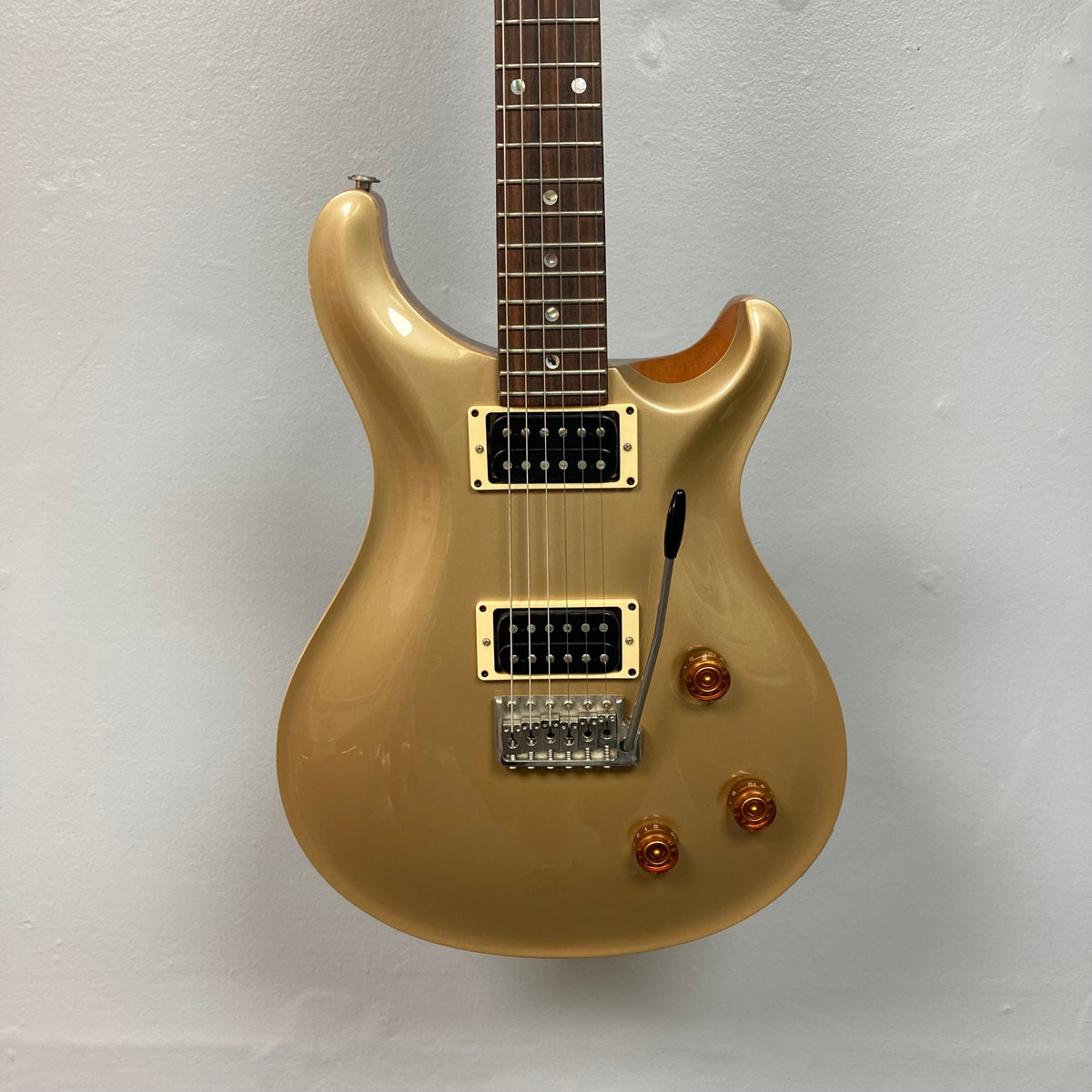 PRS 1996 Gold Top electric guitar with a gold finish, showcasing a close-up of its strings and neck, displayed on a wall.